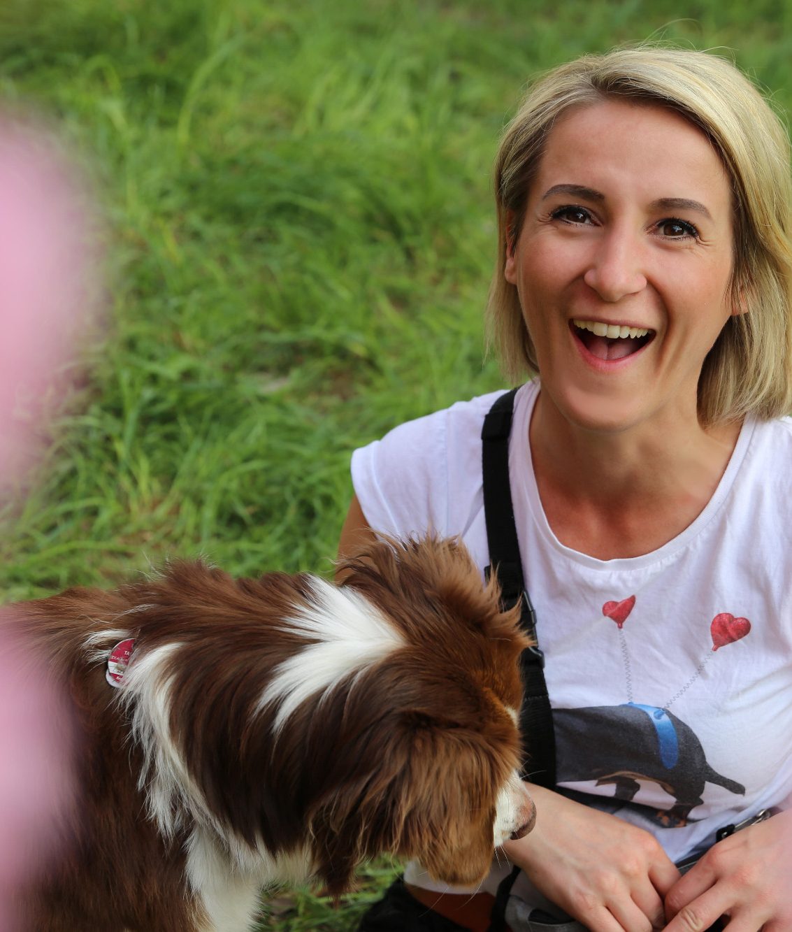 Lachende Tiersitterin sitzt auf dem Gras mit einem Hund.